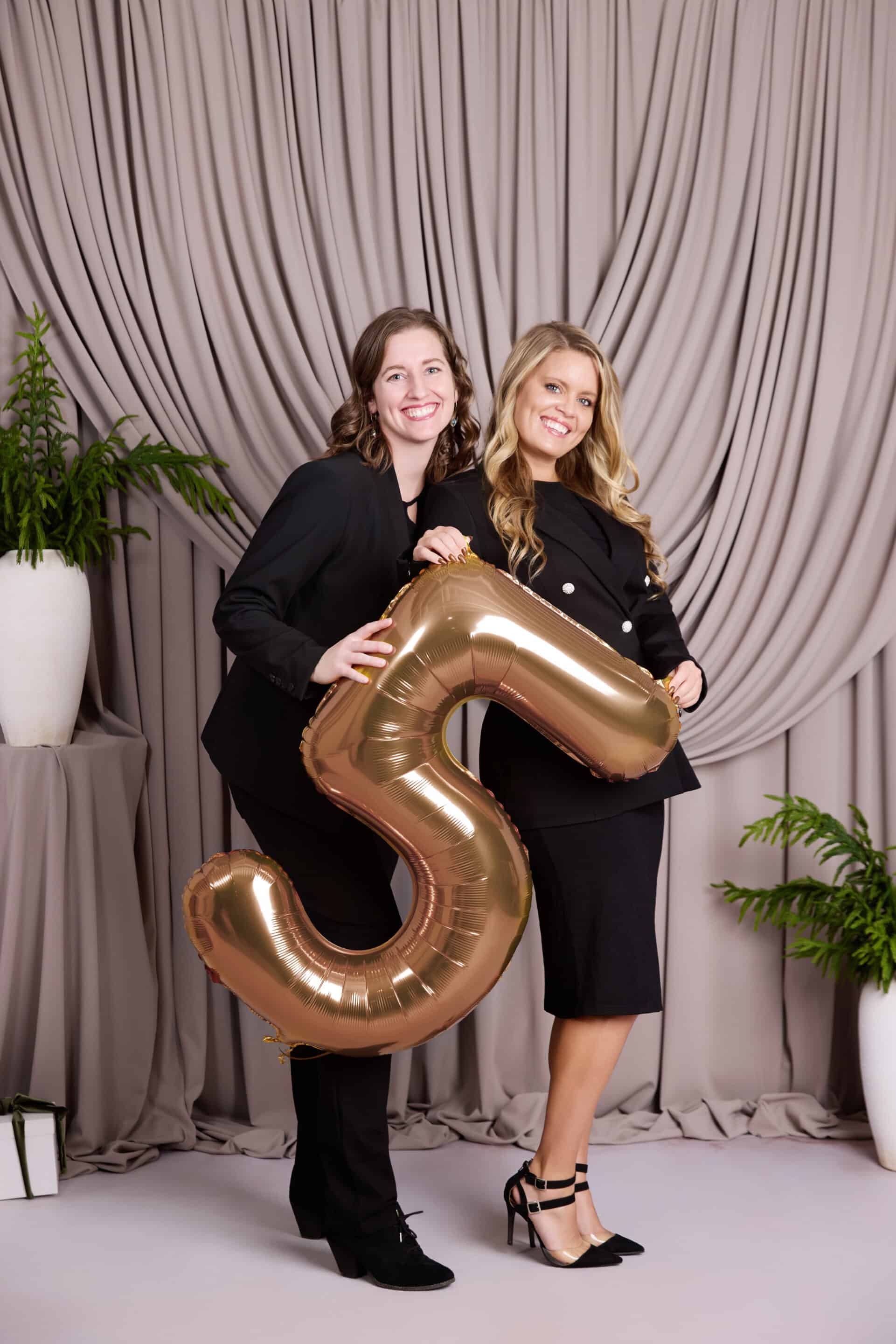 Two Rise Real Estate agents holding a golden "5" balloon
